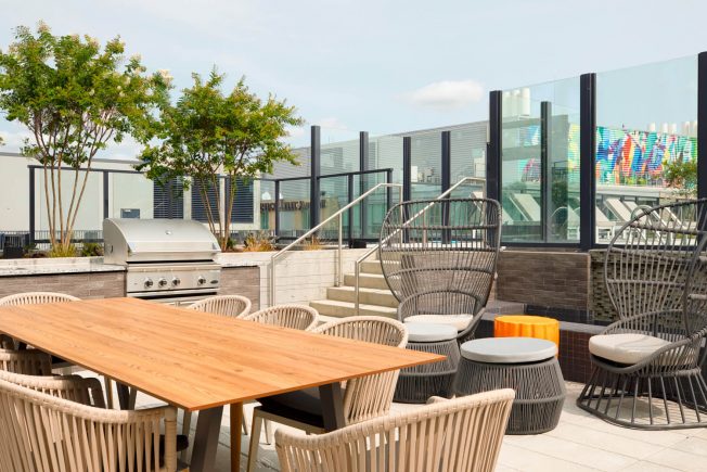Outdoor dining area on a rooftop with grill, tables, & chairs. One of the top-notch amenities at The Kelvin in Washington, DC.